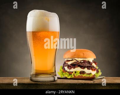 Pinta di birra lager con hamburger classico su un tavolo di legno. Foto Stock