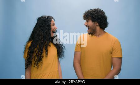 Ritratto su sfondo blu in studio coppia multirazziale diversa che si guarda l'un l'altro stupita sorpreso ridere a bocca aperta risata risposta diversa Foto Stock