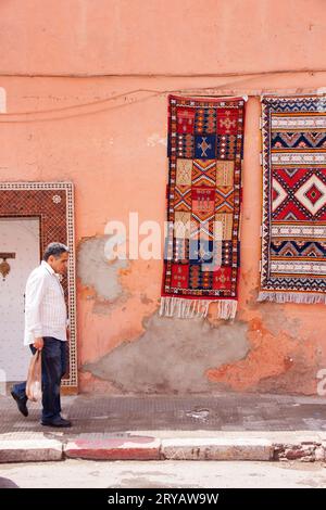 Un uomo del posto con camicia e pantaloni passeggia davanti a tappeti appesi per le strade di Marrakech, Marocco, marzo 2012 Foto Stock