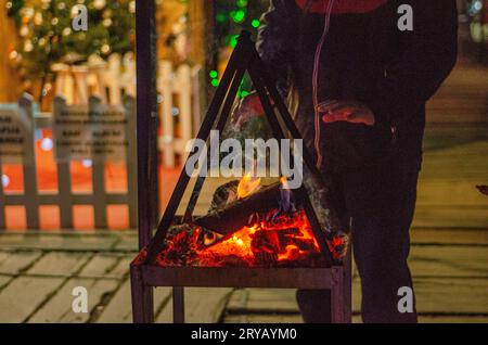 In una serata fresca, un uomo scalda le mani con il calore del caminetto Foto Stock