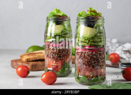 Insalata sana con quinoa, avocado, pomodoro ciliegia, ravanello, spinaci, E olio d'oliva in vasetti di Mason su fondo grigio Foto Stock