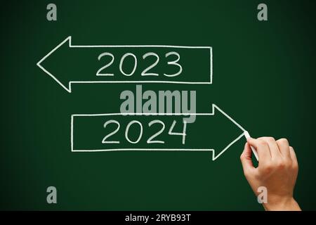 Disegno a mano felice anno nuovo 2024 addio 2023 concetto a due frecce con gesso bianco su lavagna verde. Foto Stock