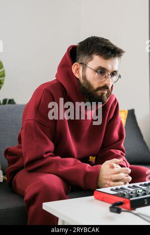 Uomo produttore di musica o arrangiatore utilizzando computer portatile e tastiera midi e altre apparecchiature audio per creare musica in casa studio. Battete facendo e organizzando Foto Stock