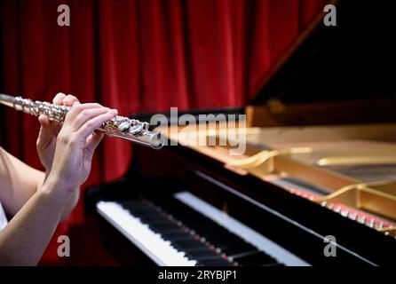 Giovani mani flautista femminili che suonano un flauto da concerto di tipo occidentale con un pianoforte a coda Steinway and Sons sullo sfondo ad Atene, in Grecia. Foto Stock