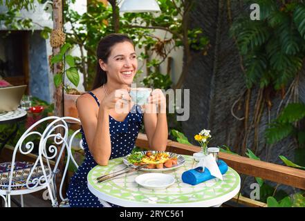 Felice donna russa di 33 anni seduta in un bar a bere cappuccino e sorridente sorridente, guardando di lato Foto Stock