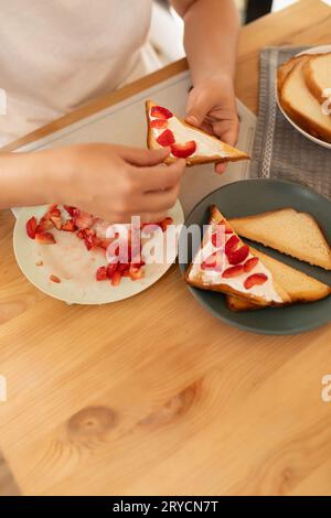 Vista dall'alto, una donna che prepara toast al formaggio spalmabile con fragole per uno spuntino Foto Stock