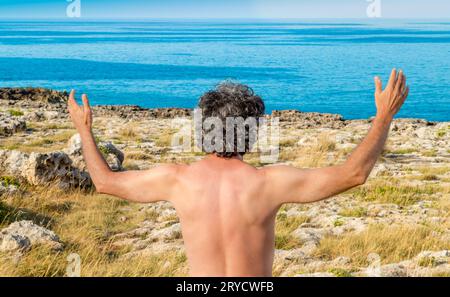 Uomo che alza le mani verso il mare Foto Stock