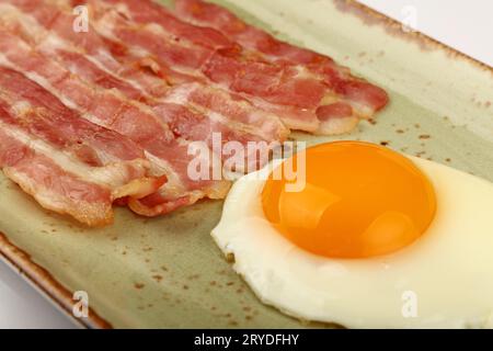 Primo piano dell'uovo sul lato soleggiato e della pancetta sul piatto Foto Stock