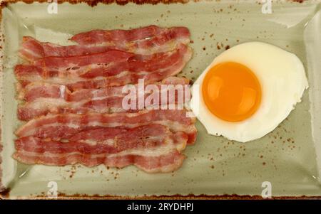 Primo piano dell'uovo sul lato soleggiato e della pancetta sul piatto Foto Stock