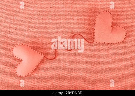 Due cuori artigianali in feltro di colore rosa corallo su tela Foto Stock