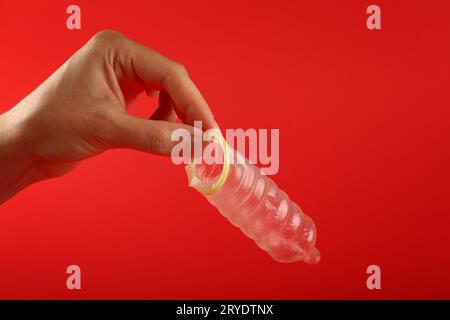 Chiudere la mano dell'uomo che tiene aperto il preservativo sopra il rosso Foto Stock