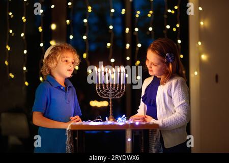 Ragazzi che festeggiano Hanukkah. Festa ebraica delle luci. I bambini accendono candele sulla menorah tradizionale. Ragazzo in kippah con dreidel e Sufganiyah Foto Stock