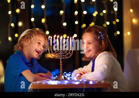 Ragazzi che festeggiano Hanukkah. Festa ebraica delle luci. I bambini accendono candele sulla menorah tradizionale. Ragazzo in kippah con dreidel e Sufganiyah Foto Stock