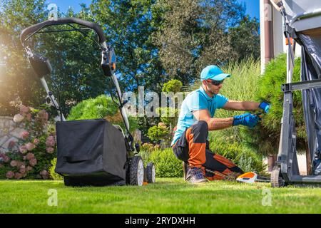 Uomo caucasico Pruning HIS Backyard Garden piante durante il clima soleggiato senza nuvole Foto Stock