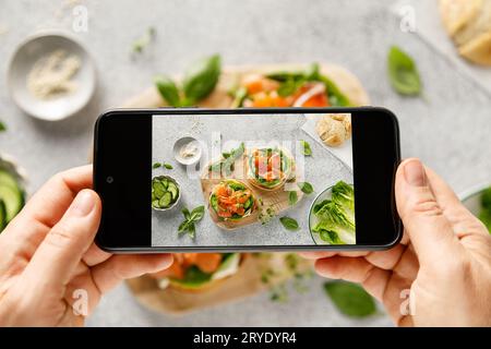 Mani femminili che scattano foto con smartphone di un sano panino con salmone salato, formaggio cremoso, lattuga verde romaina e cetriolo fresco per la pausa Foto Stock