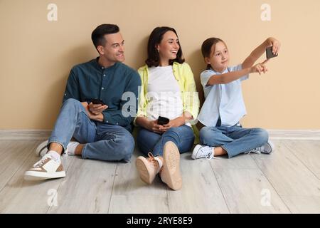 Famiglia felice con i telefoni cellulari seduti vicino alle pareti beige e scattando selfie Foto Stock