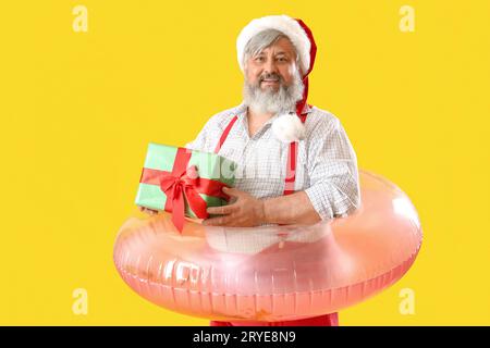 Babbo Natale con anello gonfiabile e regalo di Natale su sfondo giallo Foto Stock