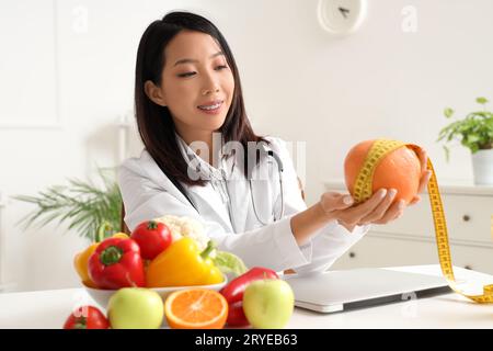 Nutrizionista asiatica femminile con pompelmo e metro a nastro in ufficio Foto Stock