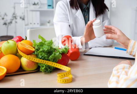 Nutrizionista femminile che consegna il flacone di pillola al paziente in ufficio, primo piano Foto Stock