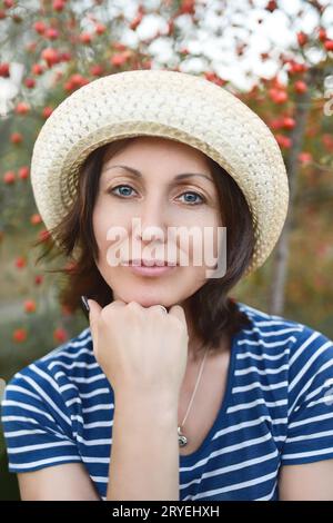 Immagine della bella donna di mezza età che indossa cappello di paglia ridendo e guardando la fotocamera mentre si cammina in estate park Foto Stock