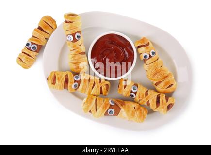 Piatto con gustose mummie di salsiccia per la festa di Halloween e ketchup isolato su bianco, vista dall'alto Foto Stock