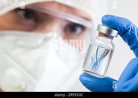 Microbiologa NHS di sesso femminile o biotecnico di laboratorio che tiene una fiala di flacone in vetro con filamento di DNA elica galleggiante in liquido Foto Stock