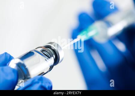 Indossare i guanti blu tenendo la siringa con l'ago inserito nella fiala con liquido antivirale Foto Stock