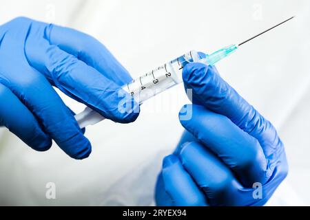 Tecnico medico, infermiere o medico che tiene la siringa nelle mani indossando guanti blu protettivi Foto Stock