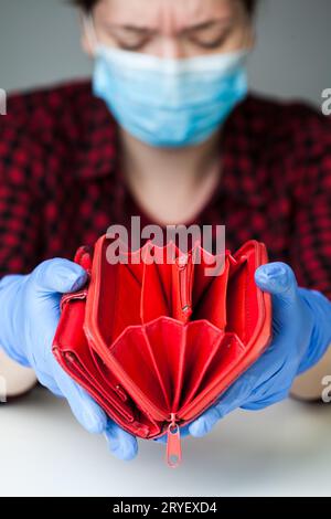 Persona caucasica femminile devastata che indossa guanti in lattice maschera medica tenendo portafoglio rosso vuoto Foto Stock