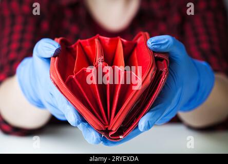 Persona che indossa guanti protettivi medici che tiene un portafoglio rosso vuoto Foto Stock