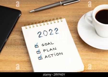 Nuovo anno 2022 obiettivo, piano, testo d'azione su blocco note e tazza da caffè e smartphone su scrivania in legno. Concetto di motivazione aziendale Foto Stock