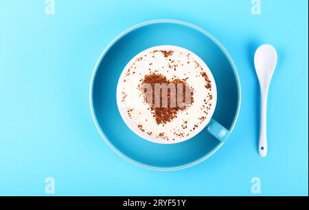 Tazza completa di caffè cappuccino con latte su carta blu Foto Stock