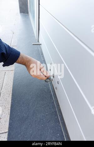 Mano con una chiave che chiude lo sportello dell'otturatore a rullo di un negozio. Concetto di chiusura Foto Stock