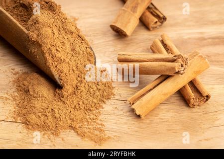 Polvere di cannella e bastoncini di cannella in paletta di legno su tavola di legno. Primo piano Foto Stock
