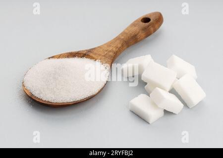 Zucchero in cucchiaino di legno e cubetti di zucchero su sfondo grigio. Primo piano Foto Stock