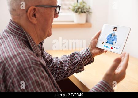 Anziano anziano che parla con una giovane medico femminile tramite una videochiamata su tablet Foto Stock