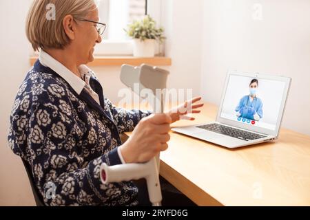 Donna anziana a casa che parla con una giovane medico femminile durante una videochiamata con un computer portatile Foto Stock