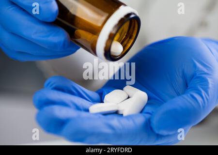 Primo piano di operatore medico o farmacista mani indossando guanti protettivi in lattice blu, versando bianco med Foto Stock