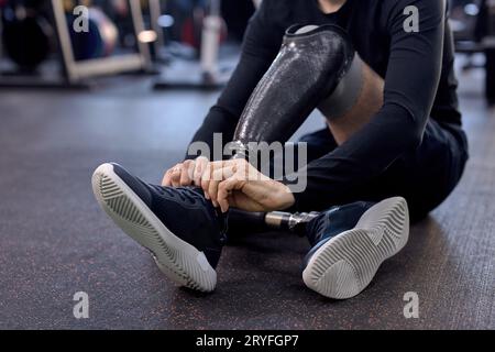 giovane sportivo con un elegante abbigliamento sportivo blu concentrato nello slegare le scarpe. primo piano foto ritagliata. concentrati sulle protesi delle gambe con le scarpe da ginnastica Foto Stock