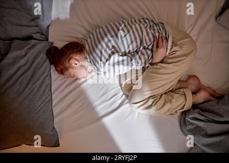 Vista dall'alto di zenzero giovane donna rossa sdraiata nel letto toccare la pancia soffre di mal di stomaco, ragazza millenaria malata lotta con periodi dolore, avere Foto Stock