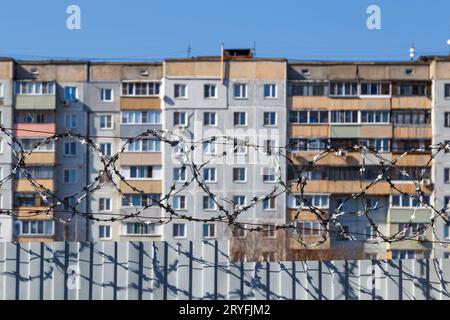 Edificio residenziale a piu' piani dietro una recinzione con filo spinato alla luce del giorno, il concetto di prigione, restrizione di liberati Foto Stock