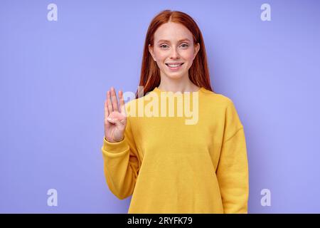 bella rossa ragazza allegra e felice, insegnante che mostra il numero 4 su sfondo blu. Alfabeto della lingua dei segni. istruzione gratuita per bambini sordi, ragazza dem Foto Stock