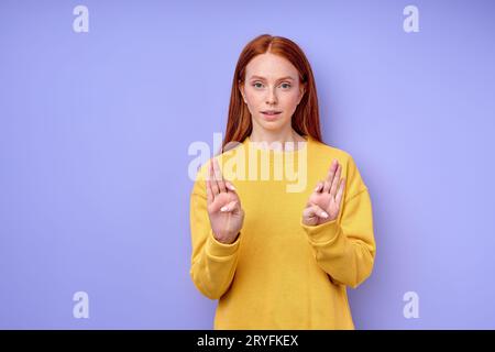 Giovane donna sorda muta a testa rossa che usa il linguaggio dei segni, spiega su sfondo blu, ritratto ravvicinato Foto Stock