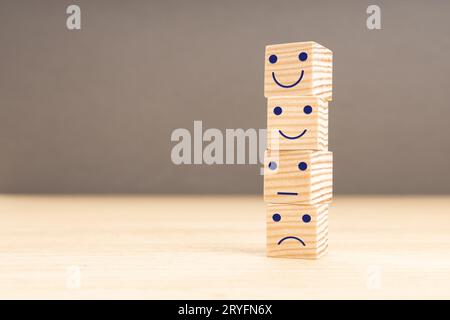 Valutazione del servizio clienti e sondaggio sulla soddisfazione. Emoticon viso su blocchi di legno impilati. Copia spazio Foto Stock