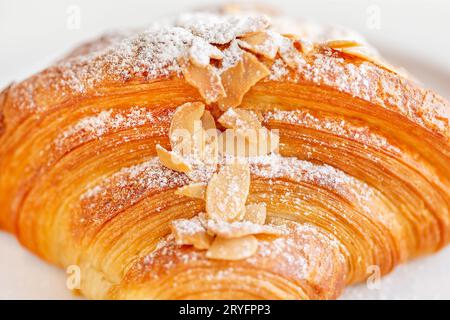 Primo piano di un delizioso croissant di mandorle fresco su un piatto, perfetto da aggiungere al caffè del mattino Foto Stock