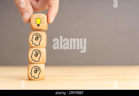 Processo di brainstorming e concetto di idea. Blocchi di legno con icona della testa a ingranaggi impilati e mano umana che tiene la parte superiore con la luce Foto Stock