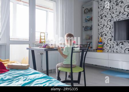 Un bambino piccolo con regali di Natale è seduto su un tavolo di legno di Capodanno con un tablet in mano. Festeggiamo il Natale. Foto Stock