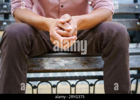 Nessuna faccia visibile. L'uomo passa del tempo seduto sulla panchina con le mani messe insieme indossando una camicia rosa. Superare i problemi, giovanotto Foto Stock