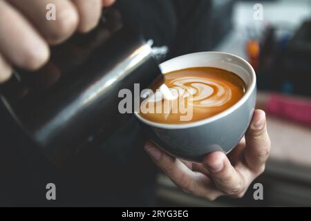 Barista che prepara il caffè latte, versando il latte in un caffè. Primo piano sulla latte art. Foto Stock