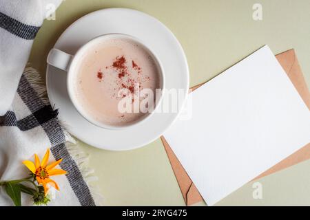 Una tazza di cappuccino piccante e carta bianca, quadri e fiori gialli su sfondo verde oliva. Vista dall'alto, base piatta, mockup. Foto Stock